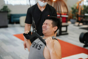 Man performing supervised strength training during physical rehabilitation or recovery, emphasizing guided exercise for musculoskeletal health and functional improvement.