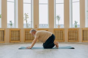 Older adult performing gentle mobility and spinal strengthening exercises on a yoga mat, supporting back health, flexibility, and rehabilitation.