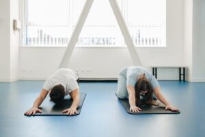 Two individuals performing restorative stretching exercises on yoga mats, promoting spinal mobility, flexibility, and guided rehabilitation for long-term musculoskeletal health.