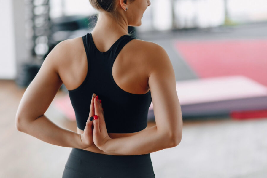 Woman in athletic wear performing a shoulder and upper back stretch in a fitness studio, highlighting flexibility, posture, and spinal mobility.