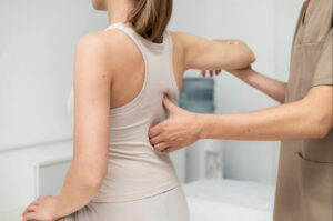 Healthcare provider performing a spinal and shoulder mobility assessment on a patient during an orthopedic or physical rehabilitation evaluation.