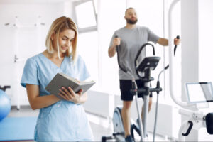 Sports medicine professional documenting patient progress while an individual performs supervised cardiovascular rehabilitation or athletic recovery training.