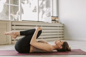 Woman performing a lower back and hip stretch on a yoga mat, demonstrating therapeutic exercise for spinal mobility, flexibility, and pain relief.