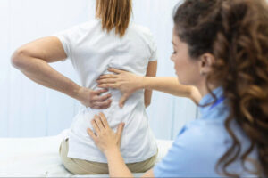 Healthcare professional assessing a patient’s lower back and spine during a physical therapy or orthopedic evaluation for lumbar pain and mobility issues.
