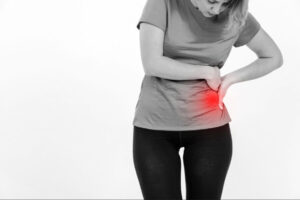 Woman experiencing hip pain with highlighted red inflammation area near the hip joint, representing symptoms that may require hip arthroplasty surgery.