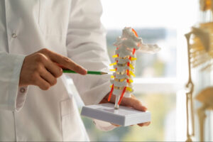 Doctor holding and pointing to a cervical spine model during a patient education session about minimally invasive spine surgery and spinal conditions.