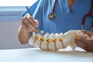 Medical professional in blue scrubs pointing to a spine model during a spinal health consultation or minimally invasive spine surgery evaluation.