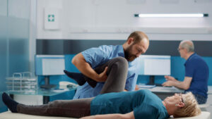 Physical therapist assisting an older patient with leg mobility exercises during post-surgical spine rehabilitation and recovery therapy.