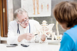 Orthopedic doctor explaining hip anatomy to a patient using a pelvis model during a post-surgical consultation about hip arthroplasty recovery and warning signs.