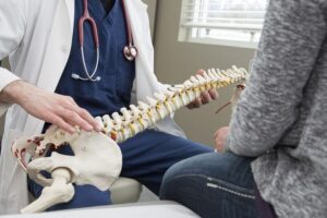 Spine specialist explaining lumbar fusion surgery using a spine model during a pre-operative consultation